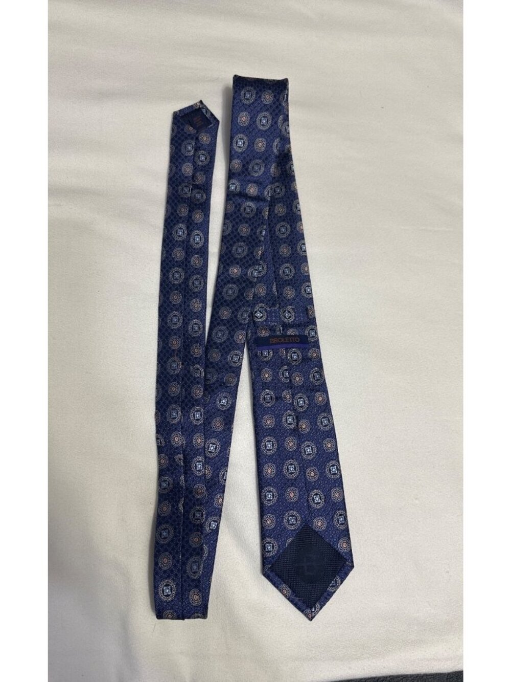 This is a 100% silk Broletto medallion necktie featuring a classic repeating geo